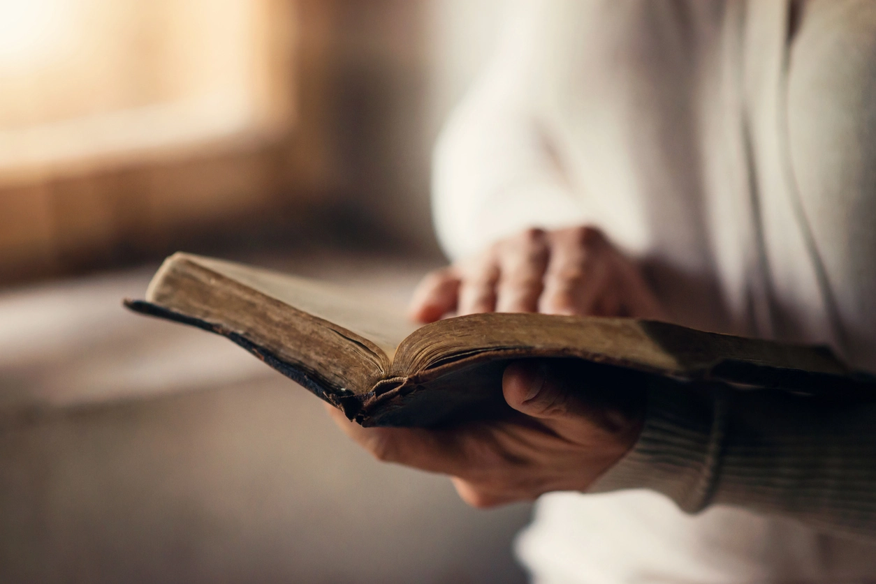 A picture of a man holding and reading the bible while standing.